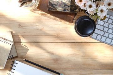 Office desk computer keyboard, coffee, flower, notebook on wooden table and morning light with top view.