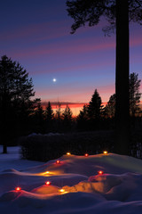 Christmas Star in winter sky at dusk. Candle lanterns glowing in the snow.