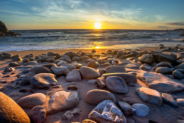 Sticker - une plage avec des pierres en premier plan, face à un coucher de soleil sur l'océan