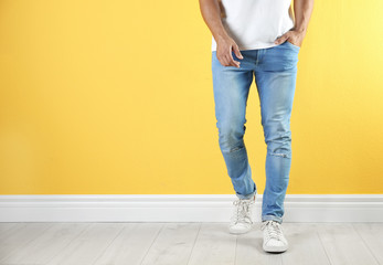 Young man in stylish jeans near color wall with space for text, focus on legs