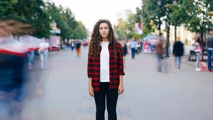 zoom in time-lapse of beautiful girl with long curly hair standing in street looking at camera when 