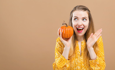 Wall Mural - Young woman holding a pumpkin on a brown background