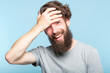 facepalm. happy smiling joyful man covering his face. shame and embarrassment concept. portrait of a young bearded guy on blue background. emotion facial expression.