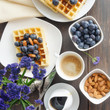 Belgian waffle decorated  with blueberries and nuts, cup of coffe on wooden background. Top view. Good morning concept square image.