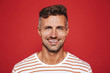© Drobot Dean - Happy attractive man with stubble in striped t-shirt smiling on camera, isolated over red background