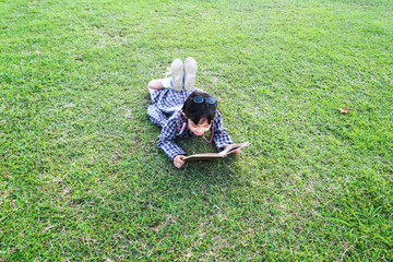 Wall Mural - little girl with glasses lying on the grass reading a book in garden at summer time