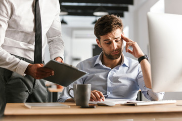 Sticker - Displeased man sitting in office working with computer near his colleague who showing clipboard with documents.