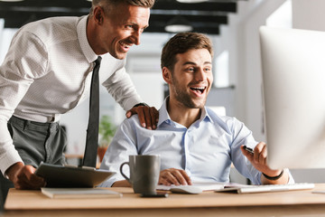 Wall Mural - happy emotional men colleagues in office working with computer.