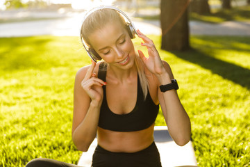 Wall Mural - Blonde sports woman in park outdoors listening music with headphones.