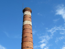 Red Brick Pipe On The Background Of The Blue Sky With White Clouds. Concept Of Idle Plant Or Environmentally Friendly Production