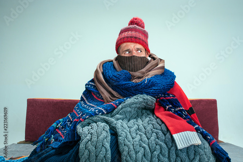 Fotografía Bearded sick man with flue sitting on sofa at home or studio covered with knitted warm clothes