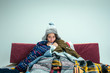 The young sick woman with flue sitting on sofa at home or studio covered with knitted warm clothes. Illness, influenza, pain concept. Relaxation at Home. Healthcare Concepts.
