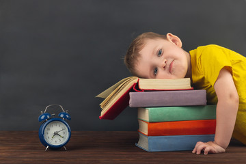 The frustrated little boy put his head on a stack of textbooks. Back to school. Doesn't want to do his homework.