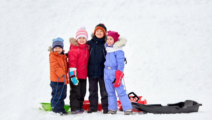 Poster - childhood, friendship and season concept - group of happy little kids with sleds hugging in winter