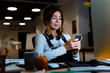 © Drobot Dean - Confused young woman designer sitting in office working using mobile phone at night.