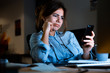 © Drobot Dean - Confused young woman designer sitting in office working using mobile phone at night.