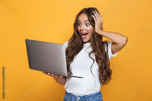 Fotomural Portrait of charming woman 20s with long hair surprising and holding gray laptop