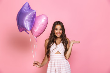 portrait of charming brunette girl 20s with long hair wearing dress smiling and holding two balloons