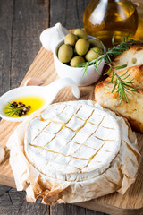 Wall Mural - Baked camembert cheese. Fresh Brie cheese and a slice on a wooden board with nuts, honey, rosemary, baguette bread grilled toasts and leaves. Brie type of cheese. Italian, French cheese.