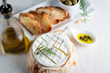 Wall Mural - Baked camembert cheese. Fresh Brie cheese and a slice on a wooden board with nuts, honey, rosemary, baguette bread grilled toasts and leaves. Brie type of cheese. Italian, French cheese.