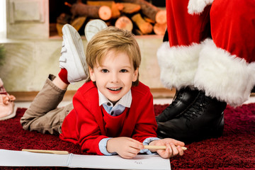 happy little kid drawing on carpet near santa