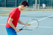 Side view of a determined Asian tennis player looking at the ball with concentration before serving during challenging match