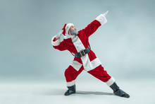 Funny Serious Guy With Christmas Hat Dancing At Studio. New Year Holiday. Christmas, X-mas, Winter, Gifts Concept. Man Wearing Santa Claus Costume On Gray. Copy Space. Winter Sales.