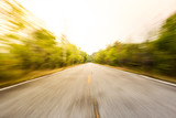 Fototapeta Natura - Photograph of asphalt road a long the forest, shot in blurred exposed lens zoom.