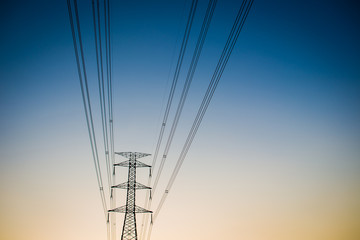 High voltage power tower close up on the worm tone sky before sunset.