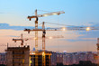 © Kekyalyaynen - Turret slewing cranes with light on frame working at sundown at evening time, buildings under construction