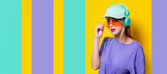 Wall Mural - Young style girl with orange glasses and headphones on colored background. Clothes in 1980s style