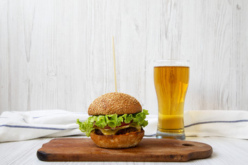 Cheeseburger and glass of beer on white wooden background, side view. Close-up.