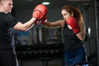 Young woman doing kickboxing training with her coach. Woman fighter ready to throw a punch with trainer teacher holding pads for boxing session