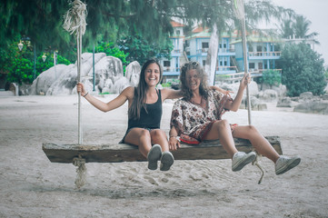 Wall Mural - Two happy girlfriend swinging on the swing at tropical beach