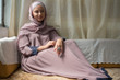 © RooM The Agency - Young woman in hijab sitting on couch