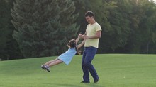 Joyful Loving Asian Father Playing With His Cute Elementary Age Daughter With Pigtails And Spinning Her While Standing On Green Lawn In Park. Carefree Family Enjoying Leisure And Having Fun In Nature.