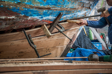 Mechanic maintenance old wood boat on beach with hand, fishery traditional Thailand bay