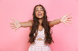 © Drobot Dean - Image of happy young woman 20s with long hair wearing dress laughing and reaching arms towards you, isolated over pink background