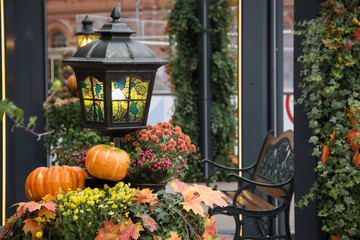 Wall Mural - Autumn outdoor decorations at the festival. Orange pumpkin and retro lantern with maple leaves,flowers and hawthorn berries. A bench metal forged in a pavilion