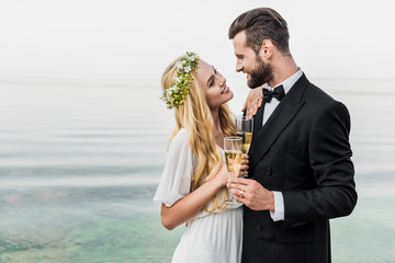 wedding couple holding glasses of champagne and looking at each other on beach