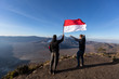 successful man hiker holding flag indonesia at cliff edge on mountain top of volcano bromo Indonesia travel at sunrise time.