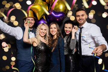 celebration, people and holidays concept - happy friends at christmas or new year party with balloons and serpentine over black background