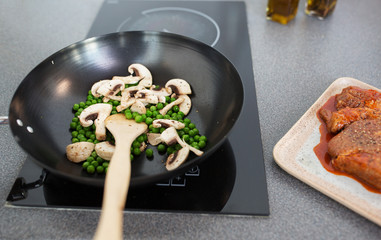 food, culinary and cooking concept - close up of mushrooms with pea in frypan on cooker