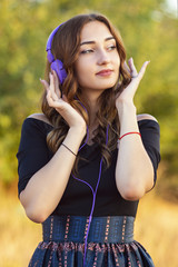 Wall Mural - portrait of a beautiful girl in headphones on head, young woman listening to music on the nature in the field