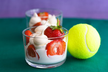 Wimbledon Inspired Whipped Cream, Meringues And Fresh Strawberries In A Glass Bowl On A Green And Violet Background With A Tennis Ball