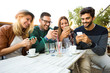 © Mediteraneo - Group of four friends having fun a coffee together. Two women and two men at cafe talking laughing and enjoying their time. Using phone