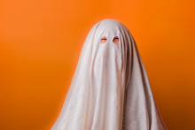 Young Child Dressed In A Ghost Costume For Halloween On Orange Background