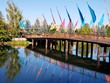 Multiple flags of a variety of brought colors in a footbridge across calm waters on the Deschutes River  that are reflecting the flags trees, and bridge. 
