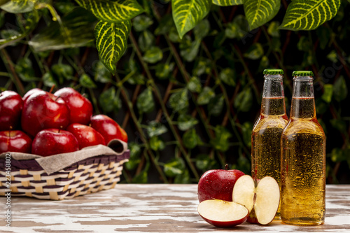 Fotografía Two bottles of nice cold cider beverage standing near braided bowl with ripe app