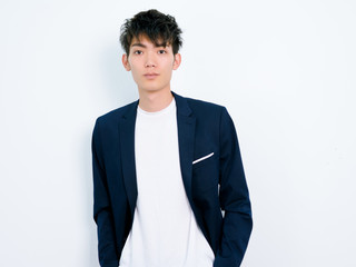 Portrait of handsome Chinese young man in dark blue leisure suit posing against white wall background. Two hand in pocket and looks confident.